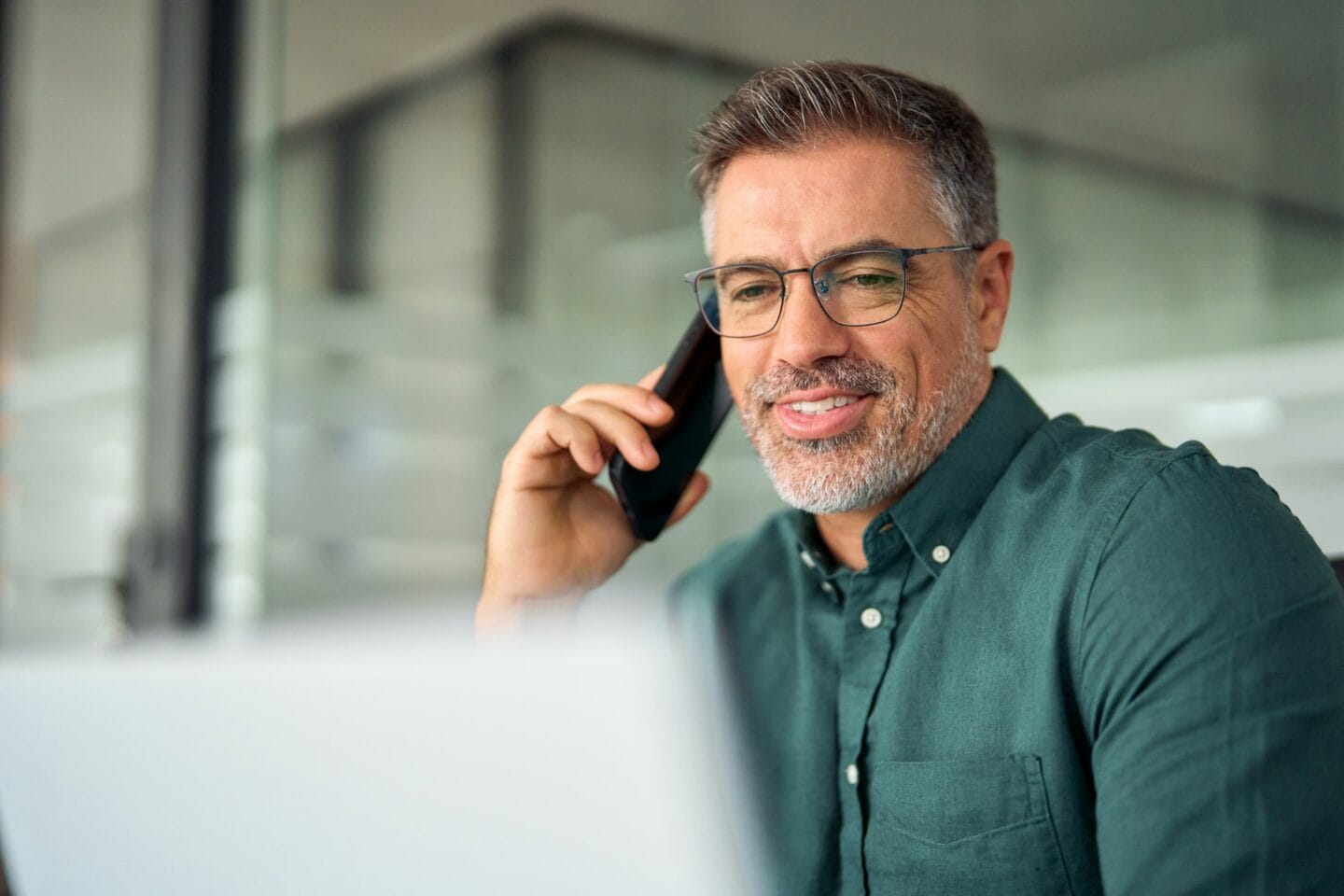 Busy older business man making phone call using laptop computer in office.