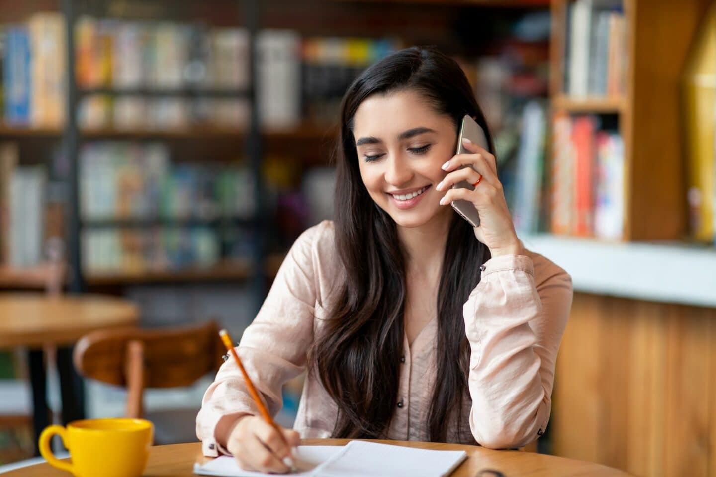 Job hunting. Happy arab woman talking by smartphone with hr representetive and taking notes, sitting